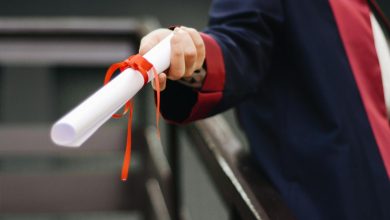 A close-up image of a graduate holding a diploma tied with a red ribbon, symbolizing achievement and success.